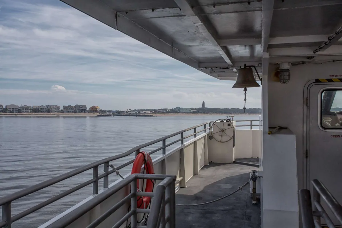 A scenic view from the deck of the Bald Head Island ferry, showing the expansive water, gentle waves, and the distant shoreline. The open-air deck invites travelers to enjoy fresh sea breezes and panoramic views as they approach the island.