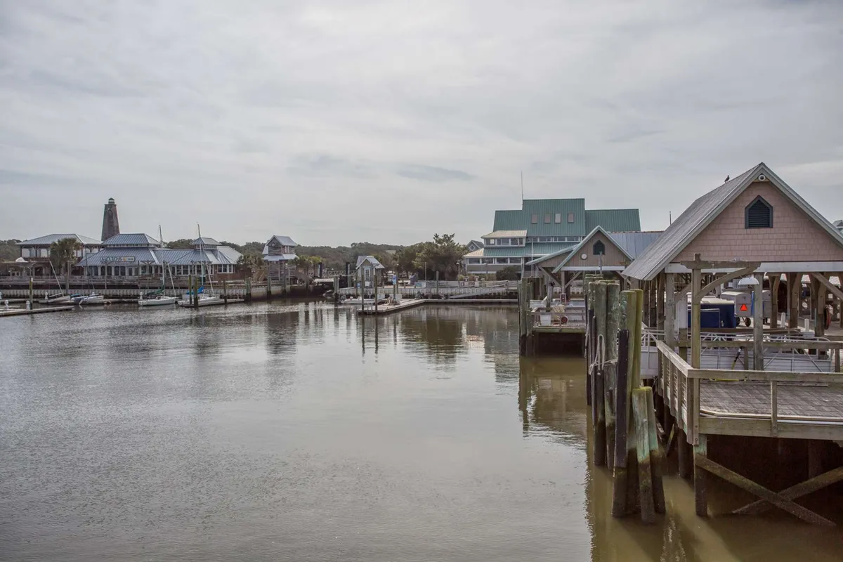 A vibrant marina scene featuring boats docked along the water, waterfront buildings, a pier, and hints of community life. The light reflects off the water as evening approaches, inviting thoughts of leisurely strolls and social gatherings near the club.