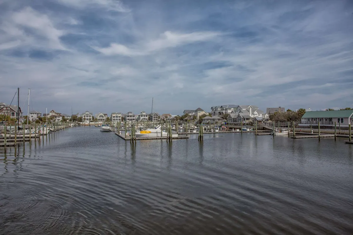 A lively marina scene featuring boats docked beside wooden piers, charming waterfront houses, and an expansive sky. The tranquil setting hints at sailing excursions and water-based adventures that are part of the island experience.