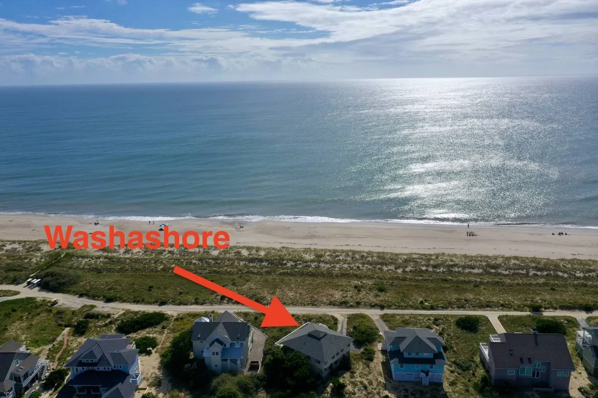 A wide-angle perspective of the expansive beach and ocean, framed by nearby houses and winding pathways. The scene invites exploration, suggesting easy access to additional nearby beaches and the freedom to set out on island adventures.