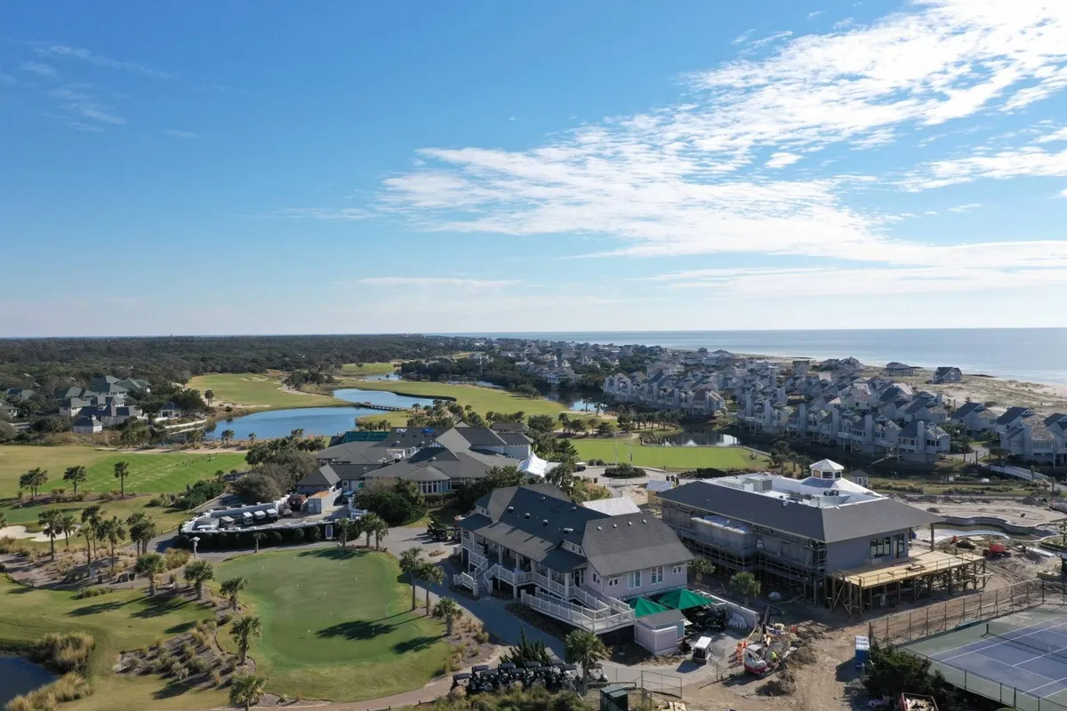 A panoramic exterior scene including a lush golf course, coastal views, residential buildings, a swimming pool, and tennis courts. The landscape is sunlit and inviting, demonstrating the leisurely and connected lifestyle available on the island.