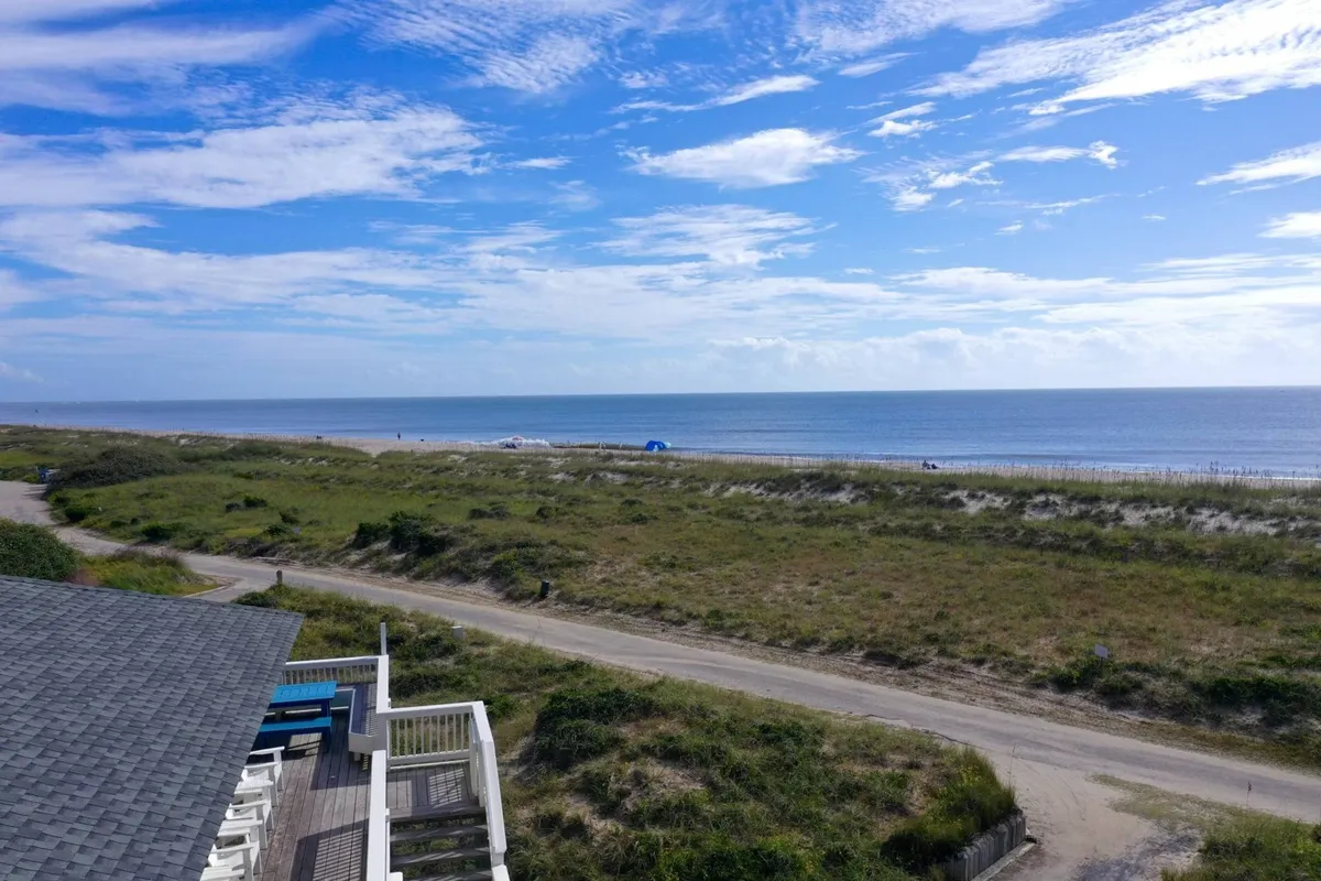 This view captures a serene stretch of sandy beach meeting the ocean under a wide sky, with gentle dunes adding natural beauty to the scene. The open, inviting shore evokes the promise of beachfront activities such as sandcastle building, sunbathing, and family fun just steps from the home.