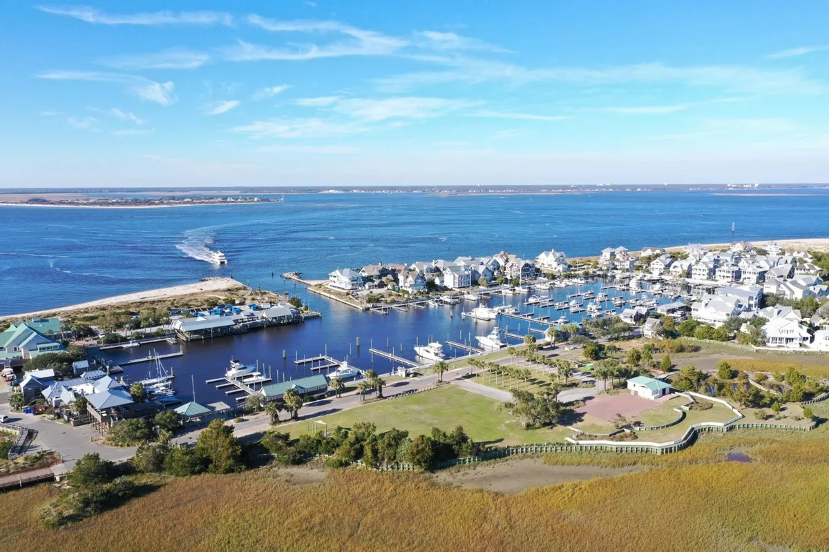 A peaceful marina scene showing waterfront houses, boats docked along the water, open green spaces, and a broad view of the marina. The waterfront is tranquil, emphasizing the island's laid-back pace and abundance of local amenities.