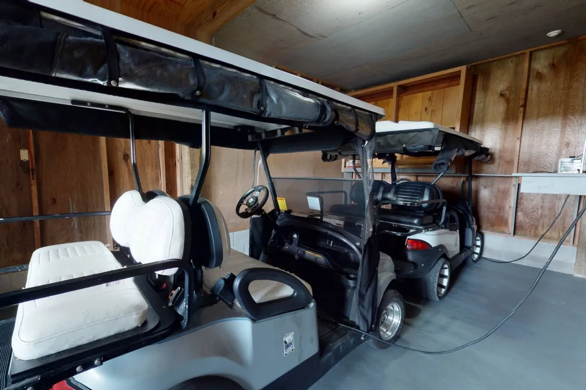 This image features a practical and organized space showcasing two golf carts parked within a wood-paneled garage, complete with a charging station. The setting highlights the readiness and convenience for guests embarking on daily island adventures.