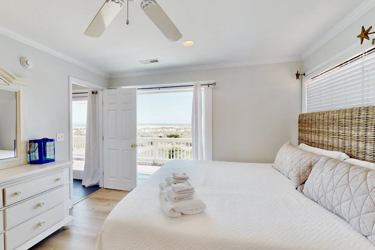A serene bedroom with two beds dressed in white linens, a window offering a glimpse of the outside, and a dresser with a mirror. The light-filled space exudes calmness, suitable for both adults and children, and reflects the flexibility of sleeping arrangements.